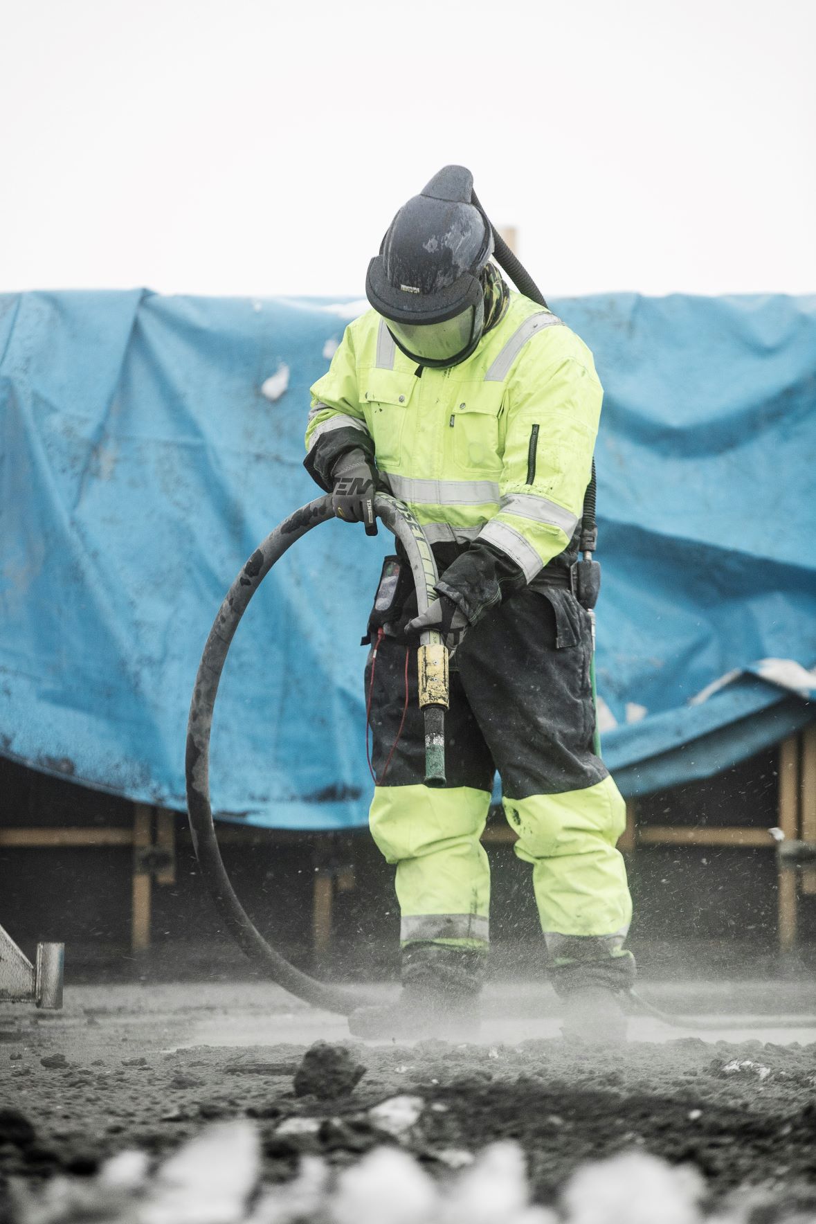 Worker in high-visibility gear sandblasting outdoors