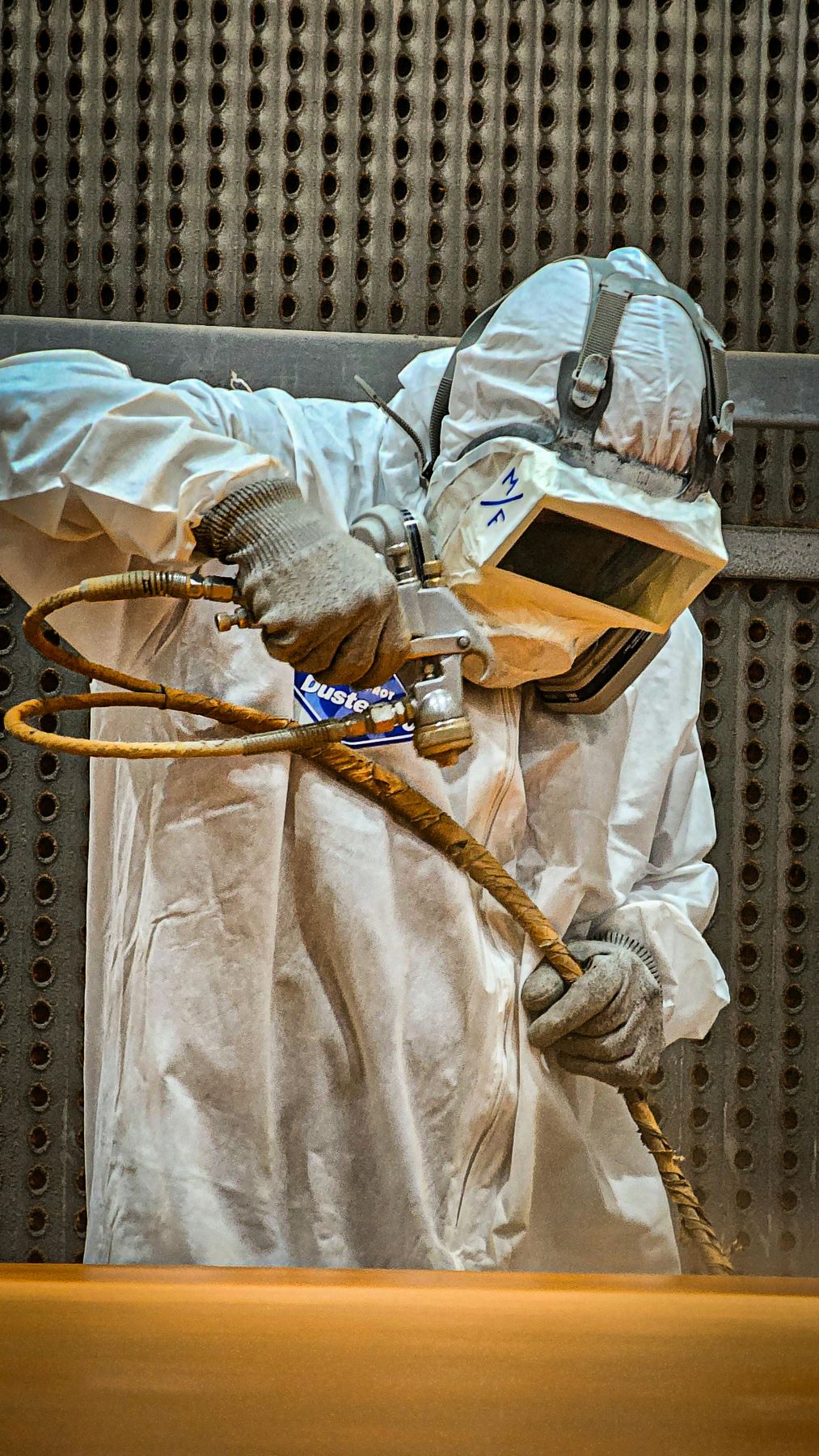 Sandblaster in protective suit blasting metal